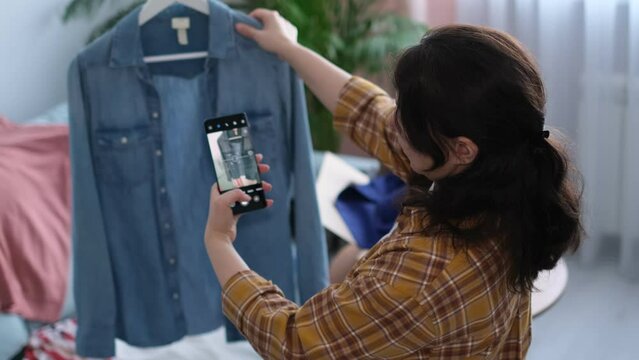 Capturing her clothing with her camera, a woman prepares her wardrobe for sale on digital flea markets. decluttering and minimalist lifestyles, the circular economy in fashion