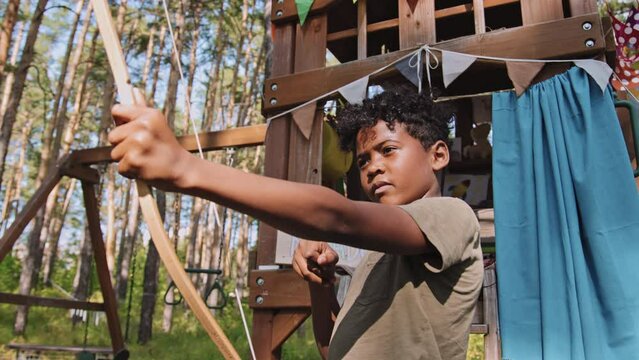 Medium shot of African American elementary age boy shooting bow on playground in forest at daytime