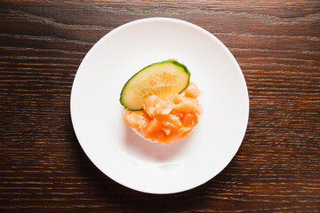 Sandwich with red fish and cucumber close-up on a white plate. Salted salmon on crispy rice bread on a wooden background
