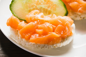 Sandwich with red fish and cucumber on a white plate close-up. Salted salmon on crispy rice bread.