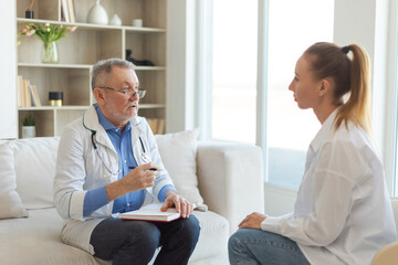 Senior man doctor examining yound woman in doctor office or at home. Girl patient and doctor have consultation in hospital room. Medicine healthcare medical checkup. Visit to doctor