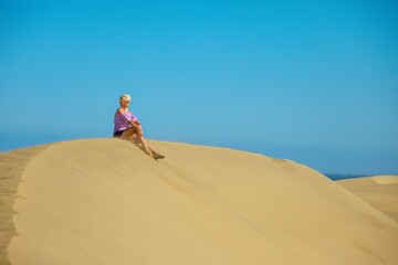 Fototapeta na wymiar tourist woman relaxing and catching tan on Maspalomas Dunes Gran Canaria.Content to relax and enjoy peaceful surroundings. Feels sense of relaxation and calm as disconnects from everyday life stresses