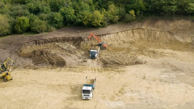 Drone shot of bulldozers and trucks working in a construction site surrounded by greenery
