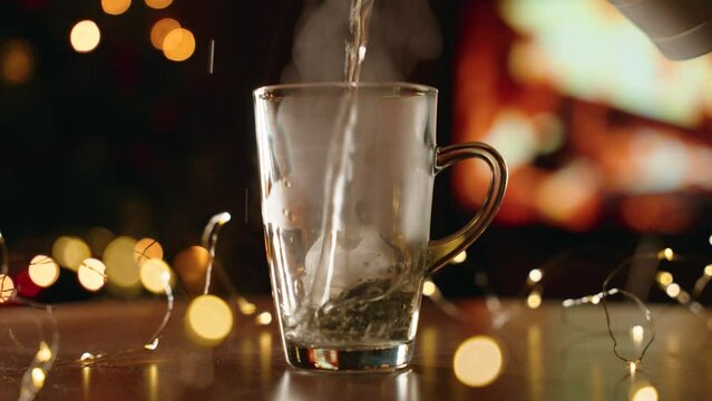 Slow-motion view of pouring hot water in a glass cup with a teabag with a bokeh lights background