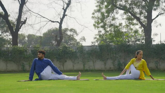 Half Spinal Twist Yoga pose or Ardha Matsyendrasana is being done by an Indian couple