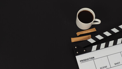 Clapper board and hot coffee white cup and two brown sugar sachet  on black background.