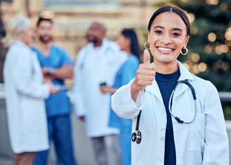 Success, thumbs up and portrait of a woman doctor with her team outdoor at the hospital. Leadership, smile and healthcare worker with an approval hand gesture with colleagues outside a medical clinic