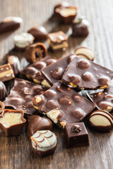 Broken chocolate bars with nuts and pralines on wooden table.