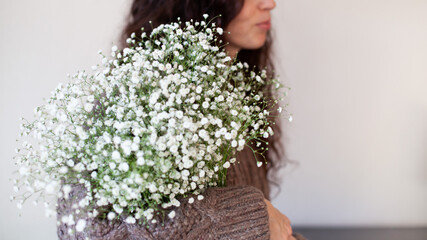 Woman wearing beige knitted sweater holding a bouquet of gypsophila flowers. Products for women,...