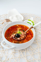 Meat solyanka. Hot combined solyanka. a portion of spicy red meat soup with tomatoes, smoked sausages and olives with lemon on a light background