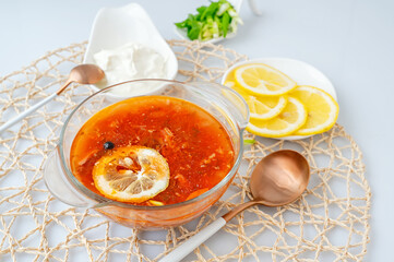 Meat Solyanka. combined solyanka. a portion of spicy red meat soup with tomatoes, smoked sausages and olives with lemon on a light background