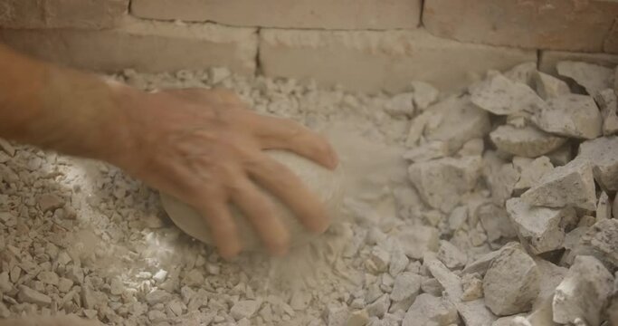 A pottery craftsman breaks clay for the production of dishes with stone in his workshop
