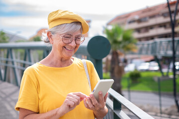 Smiling senior woman walking in the city typing a message on using smartphone. Attractive modern...