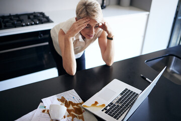 Stress, headache and business woman on laptop and coffee spill for anxiety, debt or work from home accident. Mental health problem, mistake and burnout, fatigue or tired person on computer in kitchen
