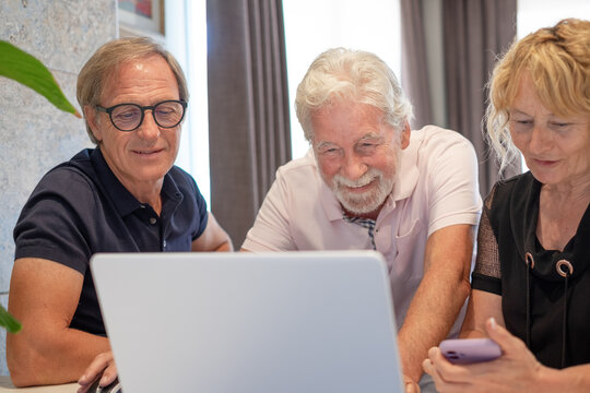 Group of mature confident business people analyzing data using together laptop computer and smartphone while spending time working from home