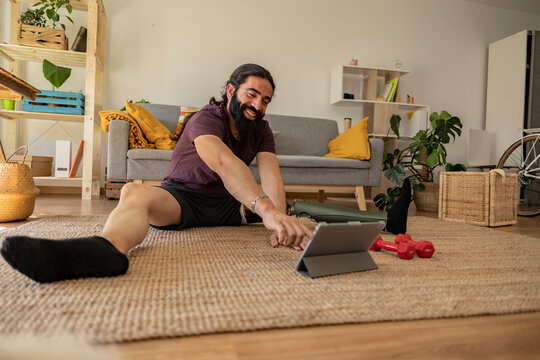 Front View Portrait Of Man With Tablet Doing Workout Exercise Indoors At Home. Has One Leg Amputated And Wears A Prosthesis