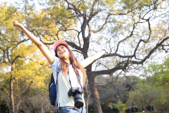 Young cheerful indian woman wearing cap and dslr camera standing with er arms open outdoor. Vacation and travel concept. Low angle