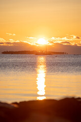 a sunset is setting over the water at the beach with the sun behind a large