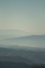 Vertical shot of the silhouettes of mountains in fog and evergreen forest trees