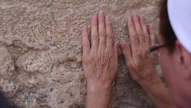Woman's hands on Western Wall with notes of paper containing written prayers and requests to God placing in cracks and crevices. Wall in old part of Jerusalem city. Tourism in Israel.