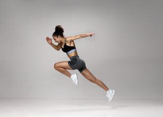 Fototapeta na wymiar Dynamic image of sportive, young, strong woman in sportswear training, running against gray studio background. Concept of sportive lifestyle, beauty, body care, fitness, health, marathon