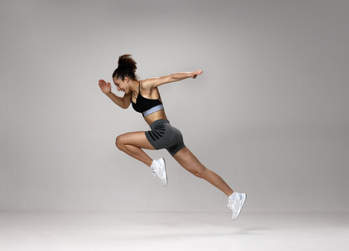 Dynamic image of sportive, young, strong woman in sportswear training, running against gray studio background. Concept of sportive lifestyle, beauty, body care, fitness, health, marathon