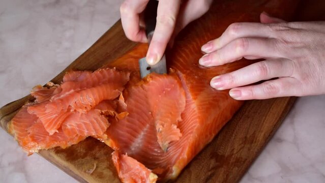 Slicing smoked trout fillet on wooden board with knife. Cold smoking red fish
