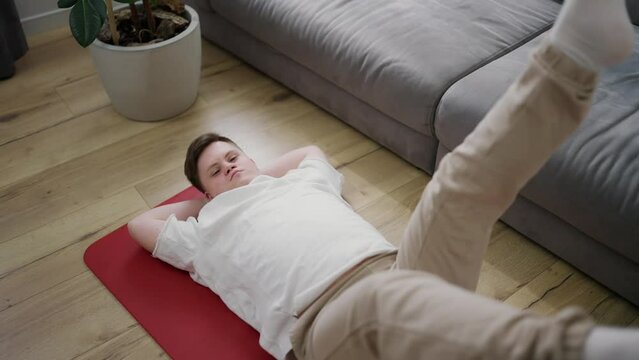 Portrait of a guy with down syndrome doing home workouts on the floor