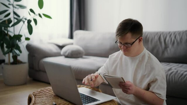 Down syndrome adult man sitting at home, using laptop for learning