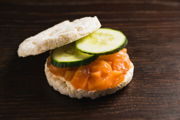Close-up, macro, sandwich with two pieces of crispy rice bread, cucumber, butter and salted salmon on dark rustic wooden background