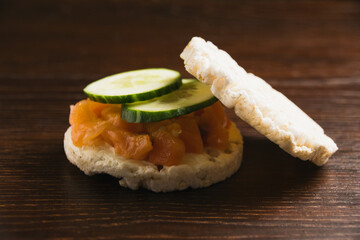 Close-up, macro, sandwich with two pieces of crispy rice bread, cucumber, butter and salted salmon on dark rustic wooden background