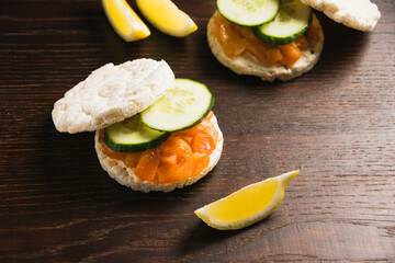 Flat lay, lemon wedges on dark background and sandwiches with salted red fish doused with lemon juice on wooden background in rustic style.