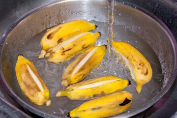 Washing yellow bananas with clean water in the aluminum bowl in the kitchen.