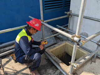 Worker and safety officer take data for gas test before confine space activity. The photo is suitable to use for industrial background and construction content media.