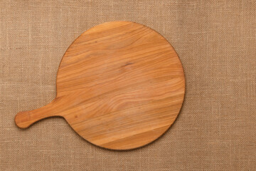Round empty wooden charcuterie serving board with handle on jute tablecloth. View from above. Minimalist flat design. Cutting board with copy space. Top view. Food template. Mockup. Cooking frame.