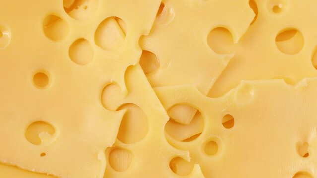 Bright yellow maasdam cheese with large holes circle rotation close up top view
