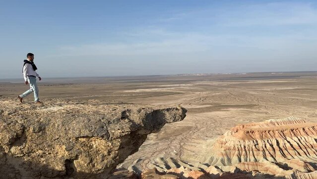 A young man walking at the edge of Yangykala Canyon, also known as a fiery fortress and crocodile's mouth.  The Plateau is located in the Balkan region of Turkmenistan.
