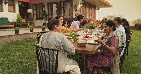 Big Indian Family Garden Party Celebration, Gathered Together at the Table in Backyard. Relatives and Friends, Young and Elderly are Eating, Drinking, Passing Dishes and Having Fun