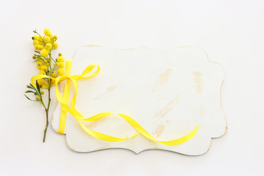 top view of yellow mimosa flowers and empty board over white background. For mock up, copy space