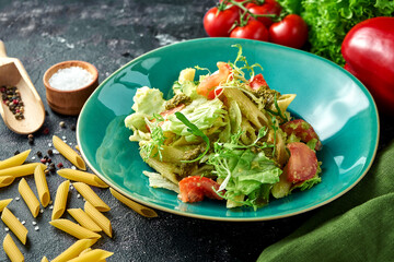 Pasta with vegetables, tomatoes and pesto in a plate on a dark background. Salad with pasta