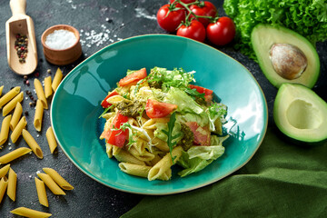 Pasta with vegetables, tomatoes and pesto in a plate on a dark background. Salad with pasta