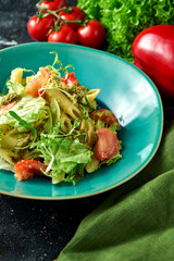 Pasta with vegetables, tomatoes and pesto in a plate on a dark background. Salad with pasta