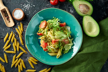 Pasta with vegetables, tomatoes and pesto in a plate on a dark background. Salad with pasta