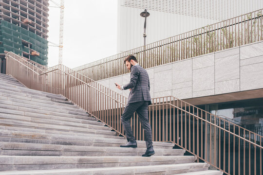 Young bearded elegant businessman going upstairs using smartphone