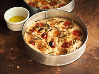 baked Focaccia bread with rosemary and tomato in round pan