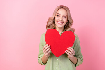 Photo of positive cute girl toothy smile hands hold red paper heart look empty space isolated on pink color background