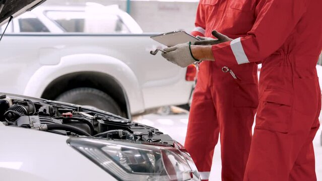 Close-up hands two-man car mechanics, they are debating talking about car being brought in for repair, holding car condition checkbook in hand ready open hood car to inspect abnormal parts.