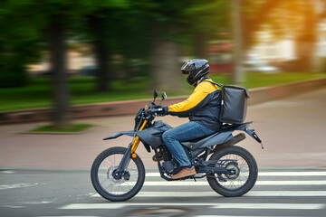 Fototapeta na wymiar Food delivery motor bike driver with backpack behind back is on his way to deliver food. Courier on motorcycle delivering food. MOTION BLUR. Shipping of goods to customers from restaurant. Takeaway