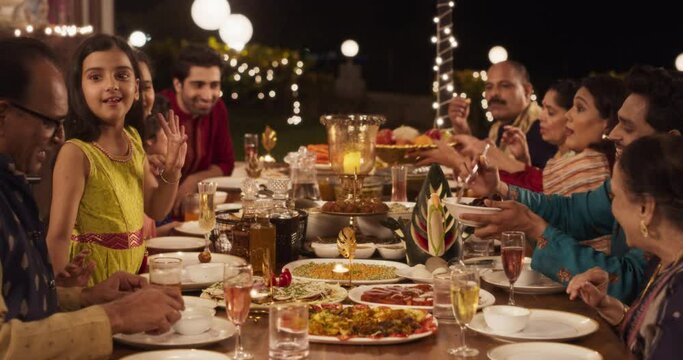 Happy Indian Family Having a Feast and Celebrating Diwali Together: Group of People of Different Ages in Their Traditional Clothes Eating Dinner Together in a Backyard Garden, Talking and Laughing