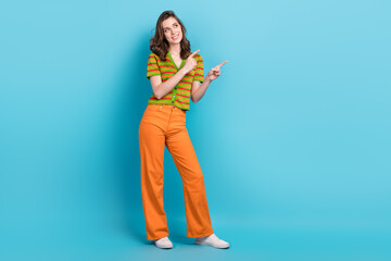 Full size photo of friendly woman dressed pants colorful cardigan directing look at sale empty space isolated on blue color background